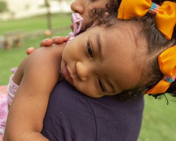 Tender moment of a mother hugging her young daughter in a sunny outdoor park.