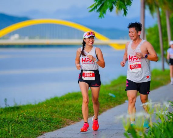 Joyful runners in a marathon passing by a distinctive yellow bridge on a sunny day.